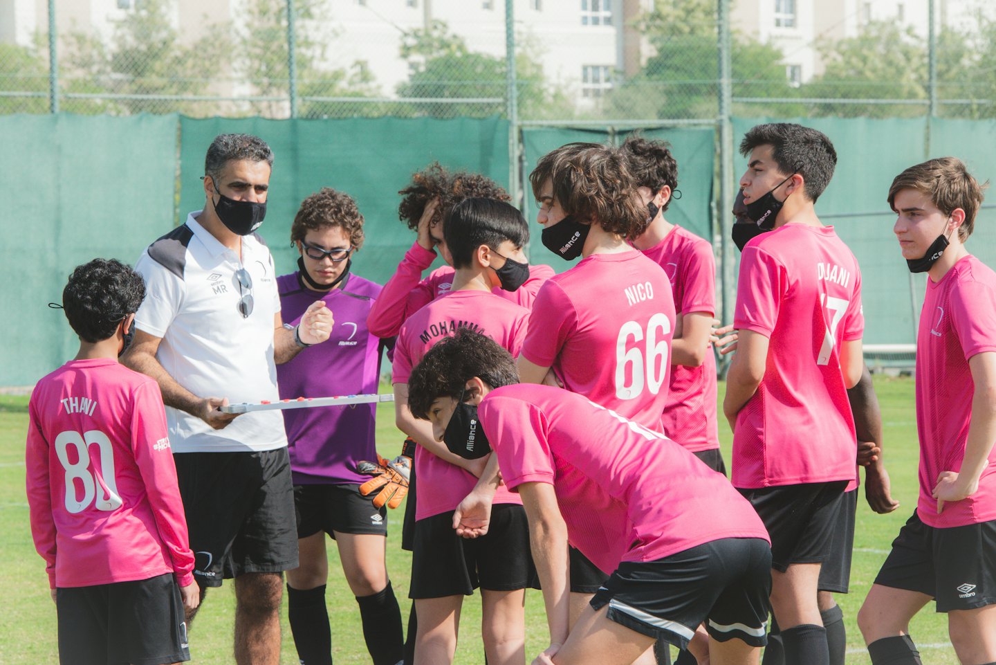 Allenatore di calcio spiega la strategia a giocatori adolescenti su un campo erboso.