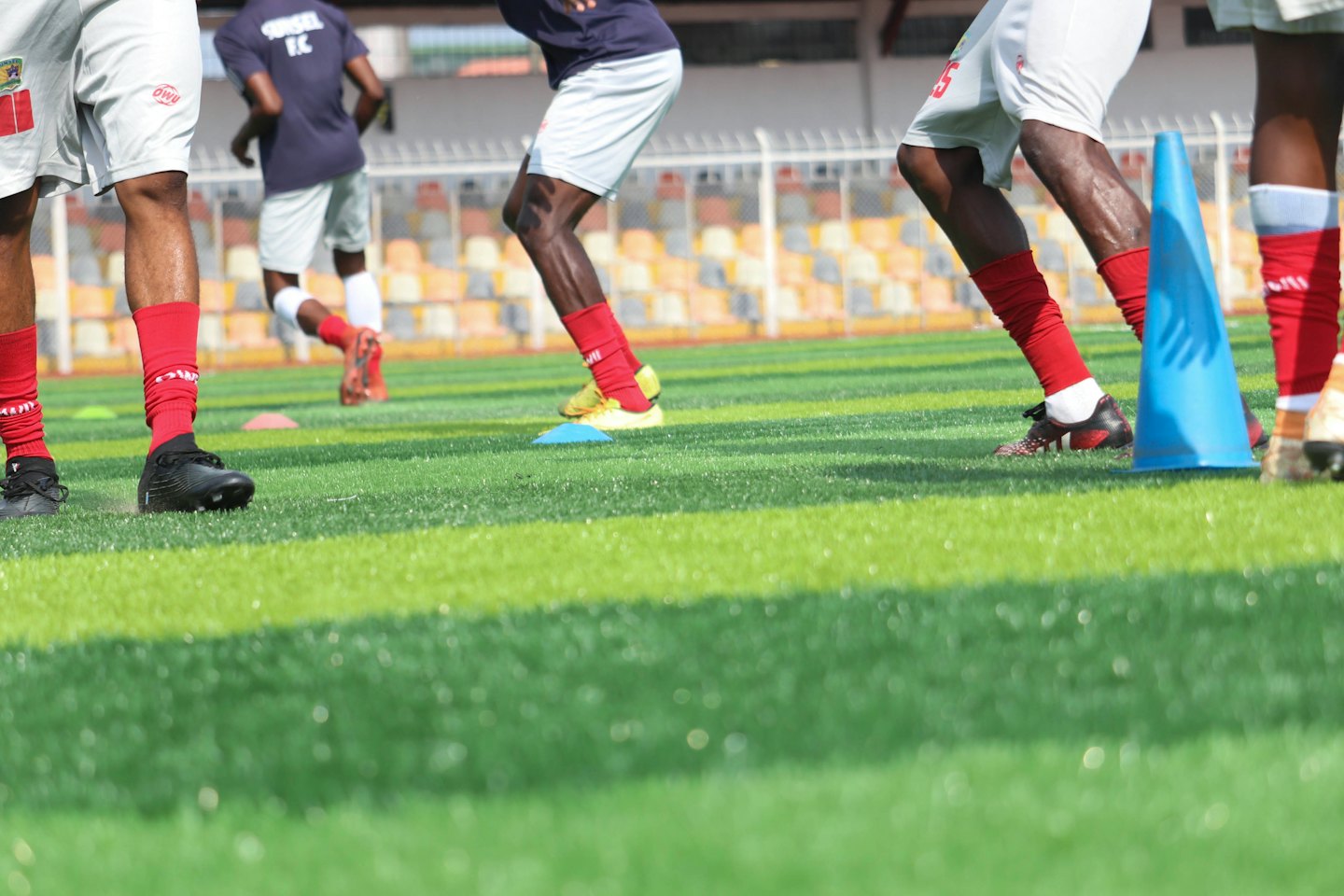 Giocatori di football in pantaloncini bianchi corrono su un campo in erba sintetica.